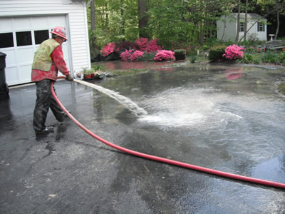 Worker washing down a residential driveway after geothermal drilling installation.