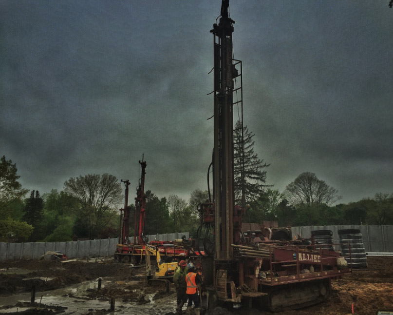Multiple geothermal drilling rigs working at West Chester University under overcast skies.